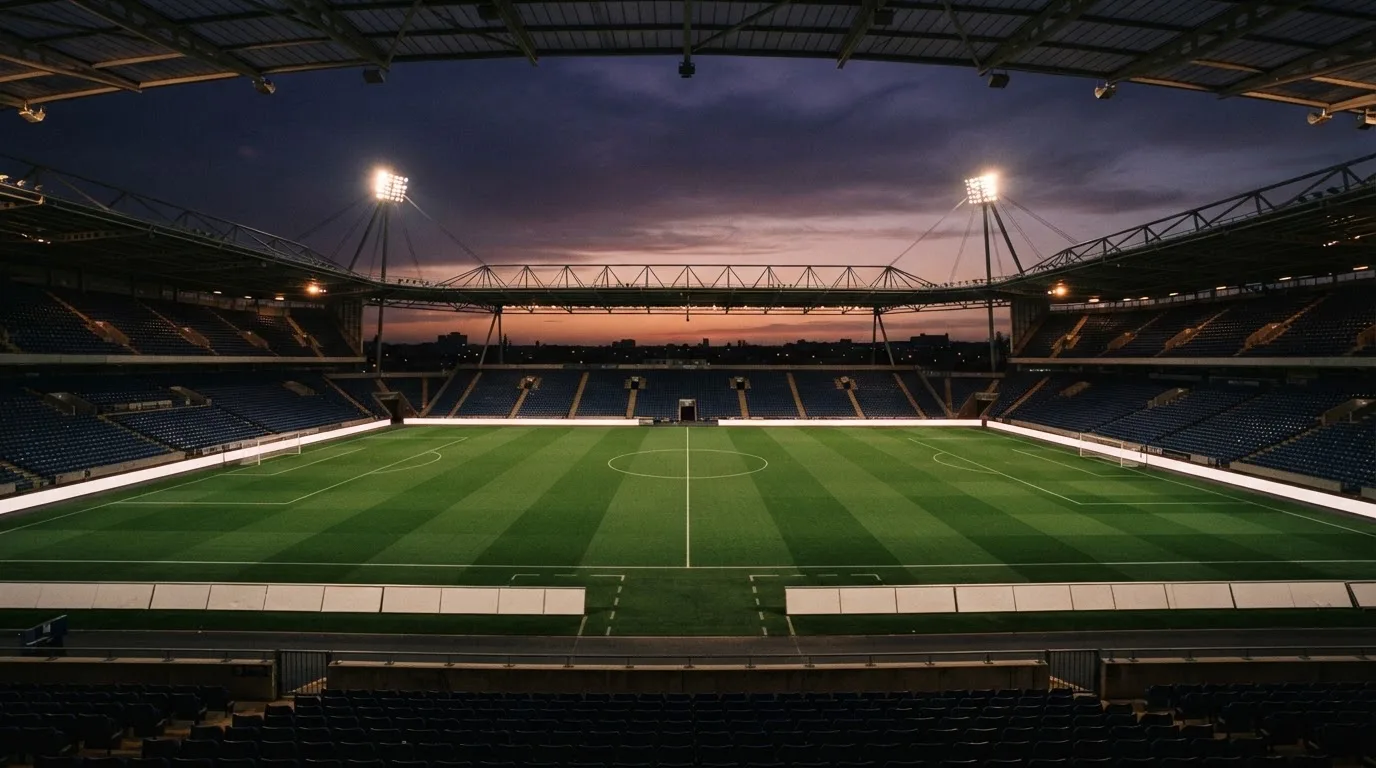 An empty football stadium with floodlight masts at dusk